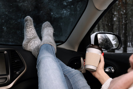 Young woman in warm socks with coffee resting inside car, closeupの写真素材