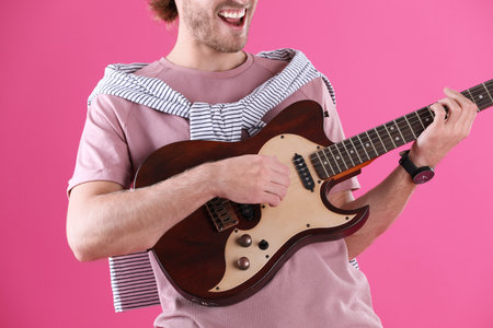 Young man playing electric guitar on color background, closeupの写真素材