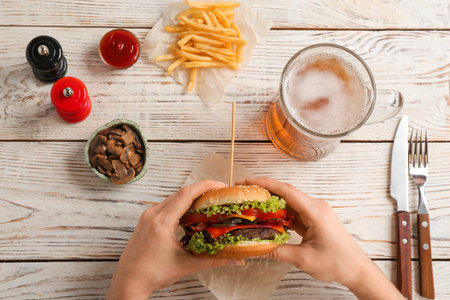 Woman holding tasty burger with bacon over wooden table, top viewの写真素材