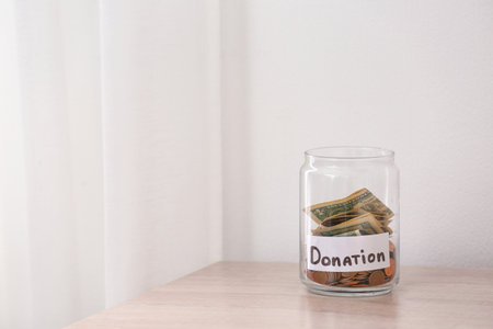 Glass jar with money and label DONATION on table against light background. Space for textの写真素材
