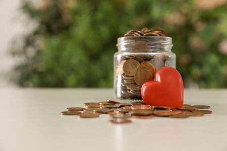 Red heart and donation jar with coins on table against blurred background. Space for textの写真素材