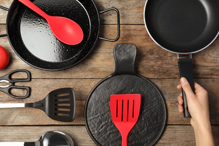 Woman holding frying pan over table with clean cookware, top viewの写真素材