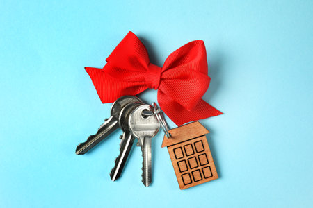 House keys with trinket and bow on color background, top view