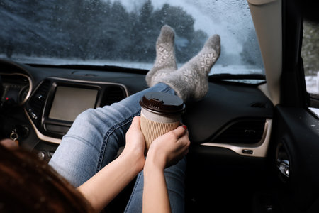 Young woman in warm socks with coffee resting inside car, closeupの写真素材