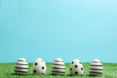 Line of traditional Easter eggs decorated with black paint on green lawn against color background,...