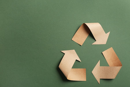 Recycling symbol cut out of kraft paper on green background, top view. Space for text