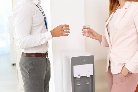Co-workers having break near water cooler at workplace, closeupの写真素材