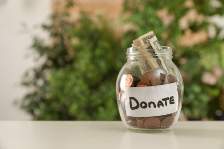 Glass jar with money and label DONATE on table against blurred background. Space for textの写真素材