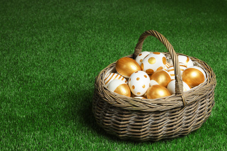 Wicker basket of traditional Easter eggs decorated with golden paint on green lawn, space for textの写真素材