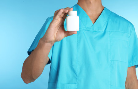 Male doctor holding pill bottle on color background, closeup with space for text. medical object
