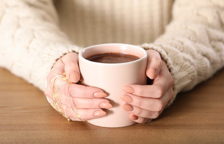 Woman in sweater holding cup of aromatic cacao on wooden table, closeupの写真素材