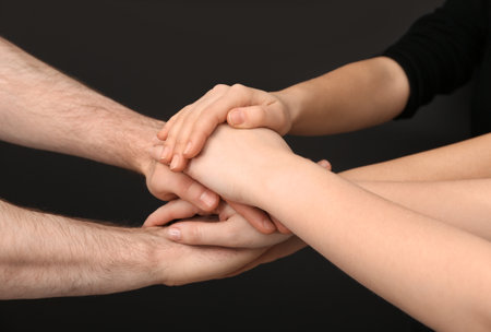 Young people putting their hands together on dark background, closeupの写真素材