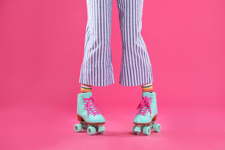 Young woman with retro roller skates on color background, closeup
