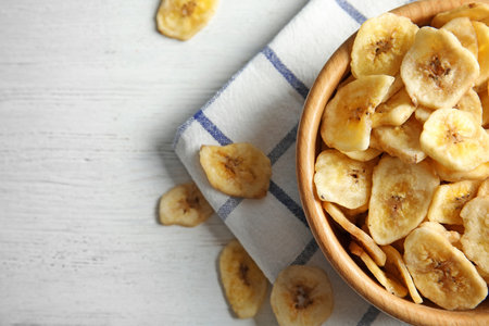 Wooden bowl with sweet banana slices on table, top view with space for text. Dried fruit as a healthy snackの写真素材