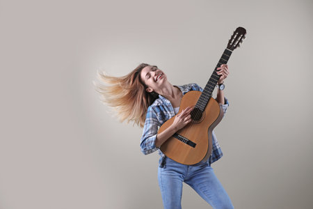 Young woman playing acoustic guitar on gray background. Space for text