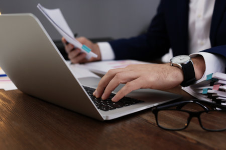 Businessman working with laptop and documents at table, closeup