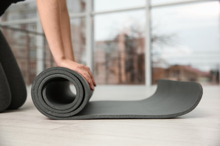 Woman rolling yoga mat on floor indoors, closeup. Space for textの写真素材