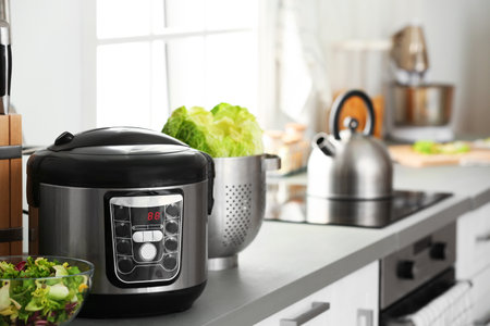 Modern electric multi cooker and food on kitchen countertop. Space for text