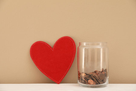 Red heart and donation jar with coins on table against color backgroundの写真素材