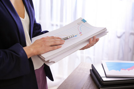 Businesswoman with stack of documents at workplace, closeup