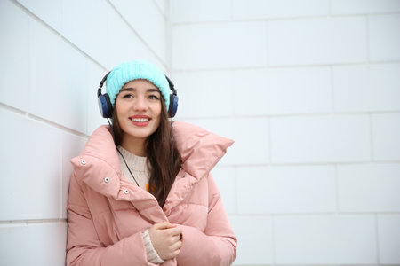 Beautiful young woman listening to music with headphones near light wall. Space for textの写真素材