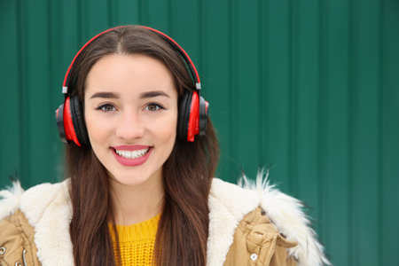 Beautiful young woman listening to music with headphones against color wall. Space for textの写真素材