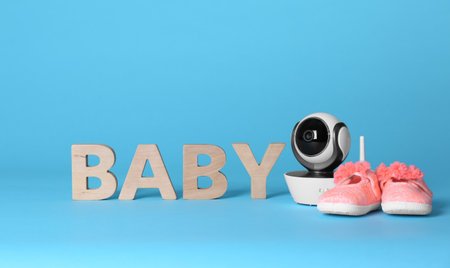 Modern CCTV security camera, small shoes and word BABY made of wooden letters on color background. Space for textの写真素材