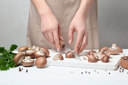 Young woman cutting fresh champignon mushrooms on wooden board, closeup viewの写真素材