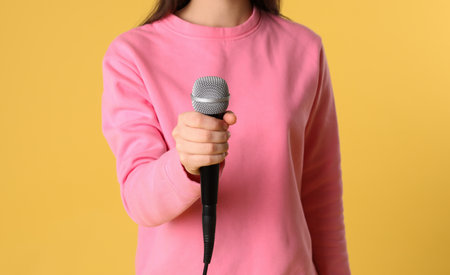Young woman holding microphone on color background, closeup viewの写真素材