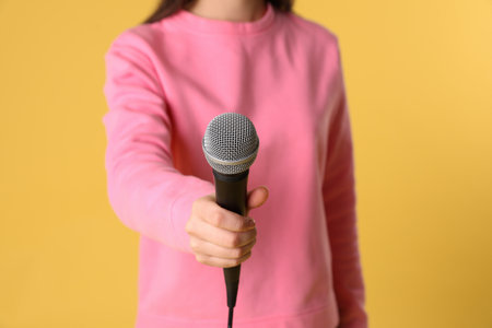 Young woman holding microphone on color background, closeup viewの写真素材