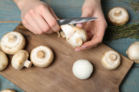 Young woman peeling fresh champignon mushrooms at table, closeupの写真素材