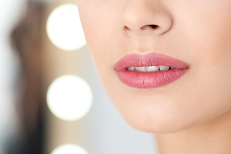 Young woman wearing beautiful lipstick on blurred background, closeup. Space for textの写真素材