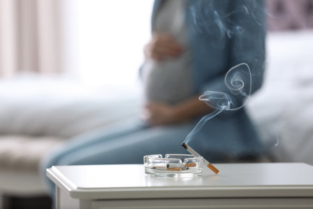 Cigarettes in ash tray and blurred pregnant woman on background, closeup. Space for textの写真素材