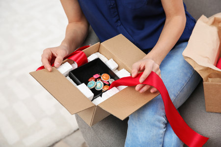 Young woman opening parcel on sofa in living room, closeupの写真素材