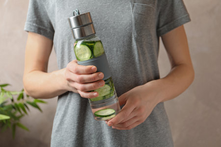 Young woman holding bottle with fresh cucumber water on color background, closeupの写真素材