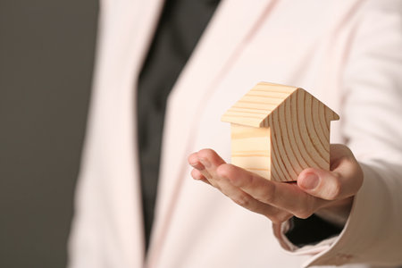 Female agent holding wooden house model on dark background, closeup. home insuranceの写真素材