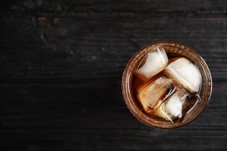 Glass of refreshing cola with ice cubes on wooden background, top view. Space for textの写真素材