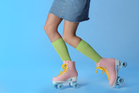 Woman with vintage roller skates on color background, closeup