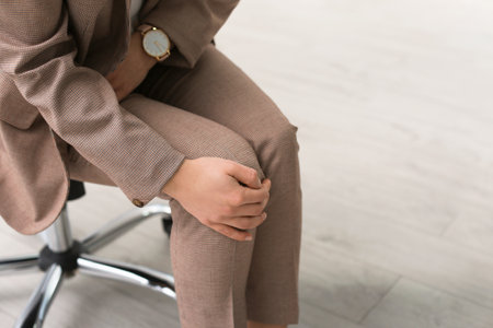 Young woman suffering from leg pain in office, closeupの写真素材