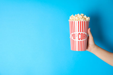 Woman holding popcorn cup on color background, closeup with space for text. cinema snackの写真素材