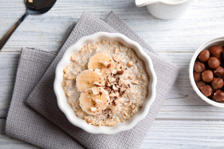 Quinoa porridge with banana and nuts in bowl served for breakfast on white wooden table, top viewの写真素材
