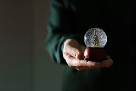 Woman holding Christmas snow globe on blurred background, closeup. Space for textの写真素材