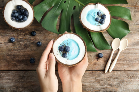 Woman holding coconut with spirulina smoothie on wooden table, top viewの写真素材