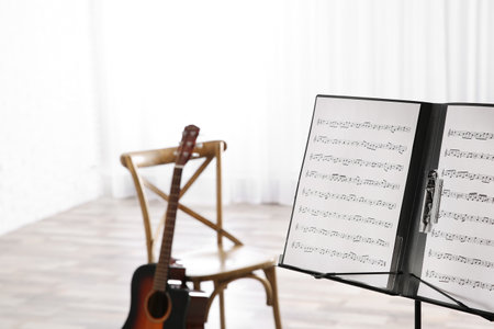 Note stand with music sheets and blurred acoustic guitar on background. Space for textの写真素材