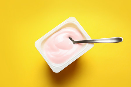 Plastic cup with creamy yogurt and spoon on color background, top viewの写真素材