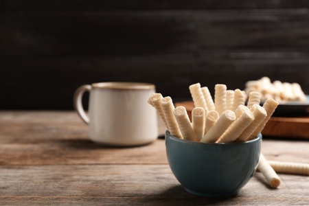 Bowl with delicious wafer rolls on wooden table, space for text. sweet foodの写真素材