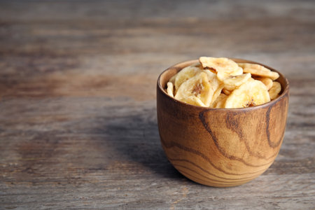 Bowl with sweet banana slices on wooden table, space for text. Dried fruit as a healthy snackの写真素材