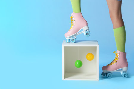 Woman wearing vintage roller skates near storage cube with balls on color background, closeup. Space...