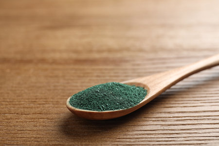 Spoon of spirulina powder on wooden background, closeup. Space for textの写真素材