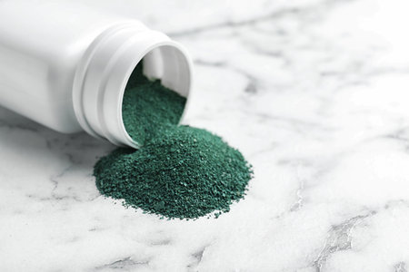 Bottle and spirulina algae powder on marble table, closeup. Space for textの写真素材